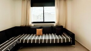 Ein modernes Wohnzimmer mit einem schwarzen Sofa, einem Fenster mit Vorhängen und Blick auf die Stadt.