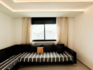 Ein modernes Wohnzimmer mit einem schwarzen Sofa, einem Fenster mit Vorhängen und Blick auf die Stadt.