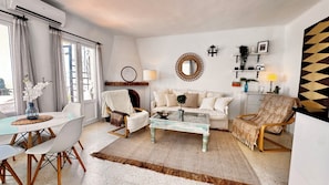 A living room with a sofa, chairs, a coffee table, a dining table with chairs, a large mirror, and a geometric wall decoration. - Panoramic sunsets in a beautiful penthouse apartment (Nerja)
