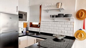Una cocina moderna con encimera negra, electrodomésticos de acero inoxidable, armarios blancos, microondas y salpicadero de ladrillo.