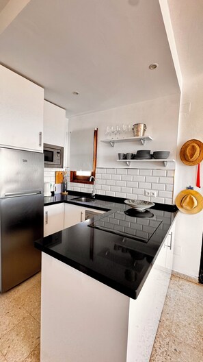 A modern kitchen with a black countertop, stainless steel appliances, white cabinetry, a microwave, and a brick backsplash. - Panoramic sunsets in a beautiful penthouse apartment (Nerja)