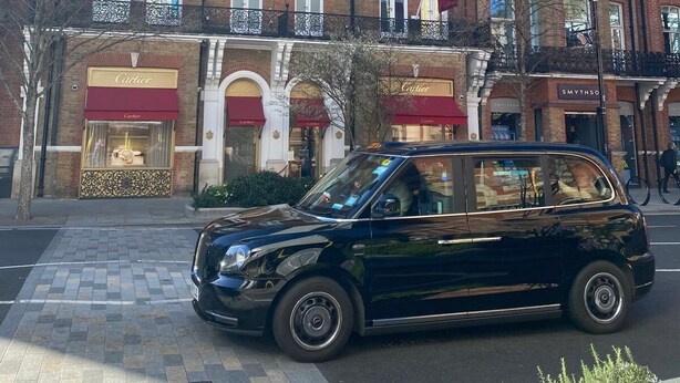 Een zwarte auto geparkeerd voor een historisch gebouw met meerdere ramen en een rode luifel.