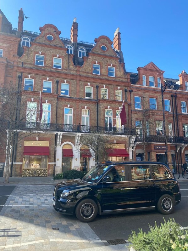 Ein schwarzes Auto parkt vor einem historischen Gebäude mit vielen Fenstern und einer roten Markise.