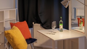 Een witte tafel met een fles en glazen, een stoel met kleurrijke kussens, en een radiator.