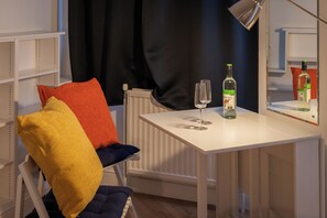 Ein weißer Tisch mit einer Flasche und Gläsern, ein Stuhl mit bunten Kissen und eine Heizung.