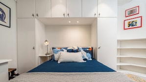 Een slaapkamer met een bed, nachtkastjes, een lamp en ingelijste foto’s aan de muur.