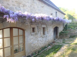 Un edificio de piedra con grandes ventanales y una puerta, rodeado de un jardín con flores moradas.