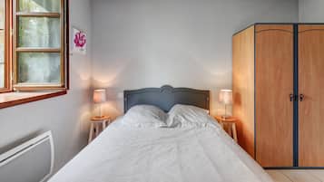 Een slaapkamer met een bed, twee bedlampen, een houten kledingkast en een raam met gordijnen.