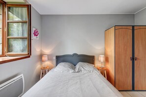 A bedroom with a bed, two bedside lamps, a wooden wardrobe, and a window with curtains.