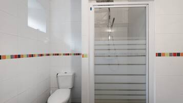 Une salle de bain comprenant des toilettes, une douche avec une porte en verre et un mur carrelé agrémenté d’une bordure colorée.