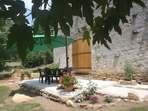 Eine Terrasse im Freien mit Steinboden, einer Holztür und einem grünen Sonnenschirm.