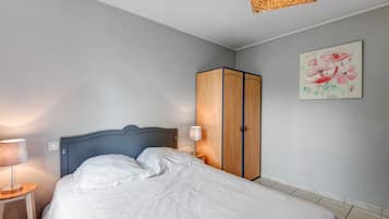 A bedroom with a bed, a wardrobe, a nightstand, a lamp, and a wall painting.