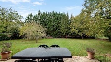 Um pátio com mesa e cadeiras, cercado por gramado e árvores.