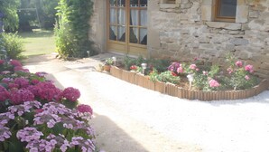 Edificio de piedra con puerta y ventanas de madera, rodeado de un jardín lleno de flores rosas.
