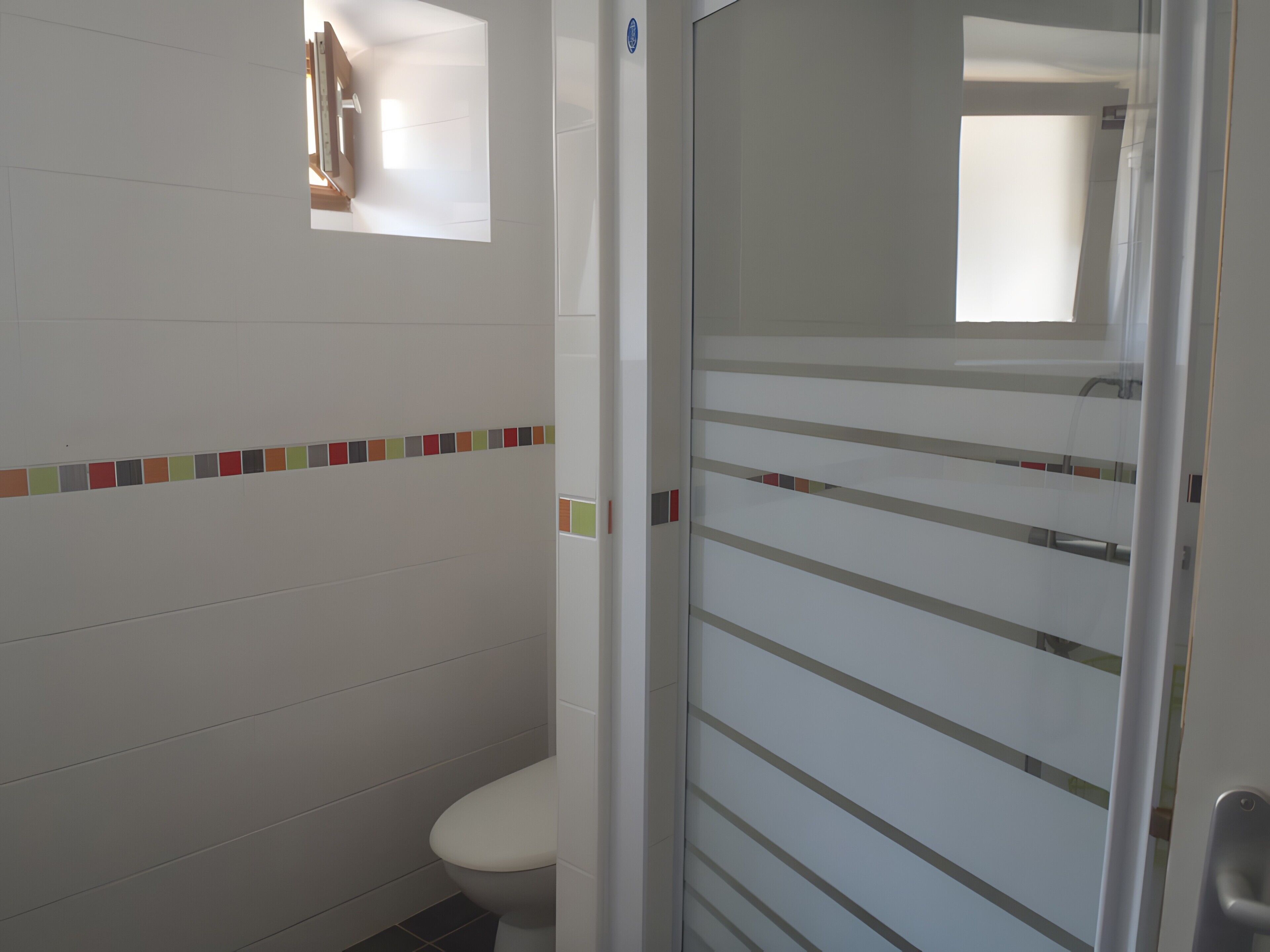 A bathroom with a toilet, a glass shower enclosure, and a tiled wall with a colorful border.