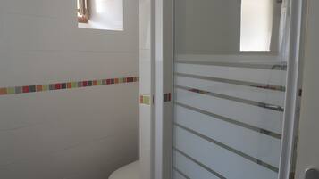 A bathroom with a toilet, a glass shower enclosure, and a tiled wall with a colorful border.