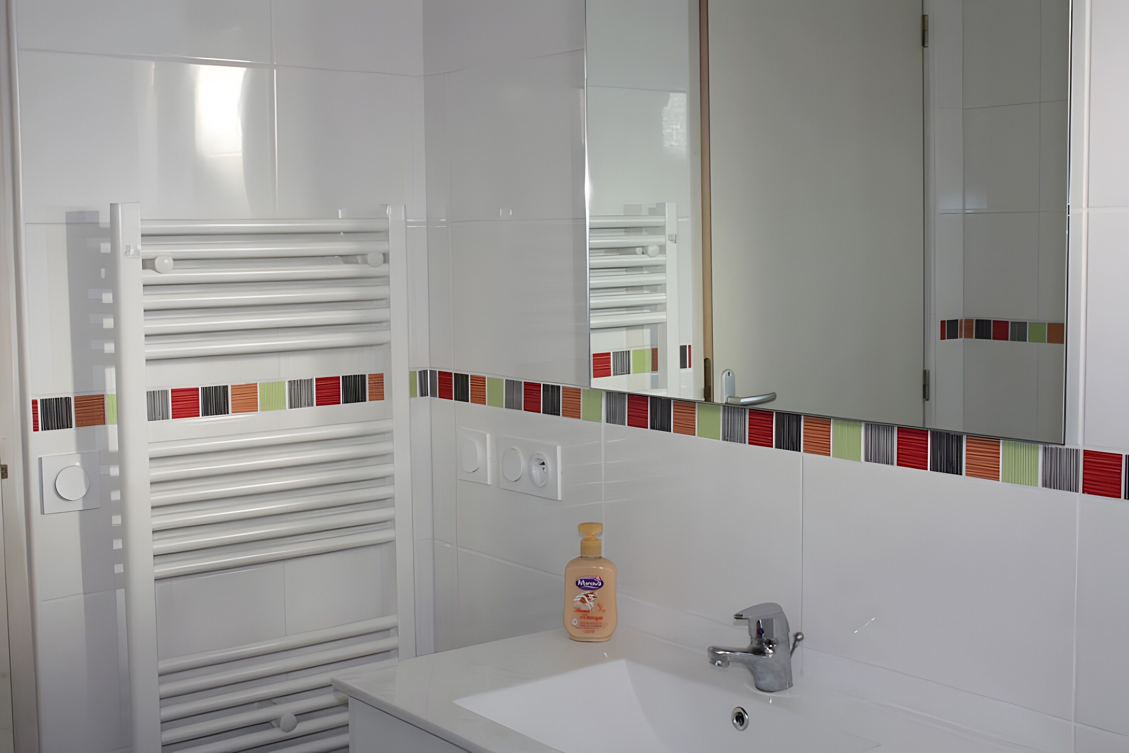 Een badkamer met een witte wastafel, een spiegel, een handdoekhouder en een flesje lotion.