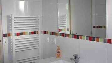 Een badkamer met een witte wastafel, een spiegel, een handdoekhouder en een flesje lotion.