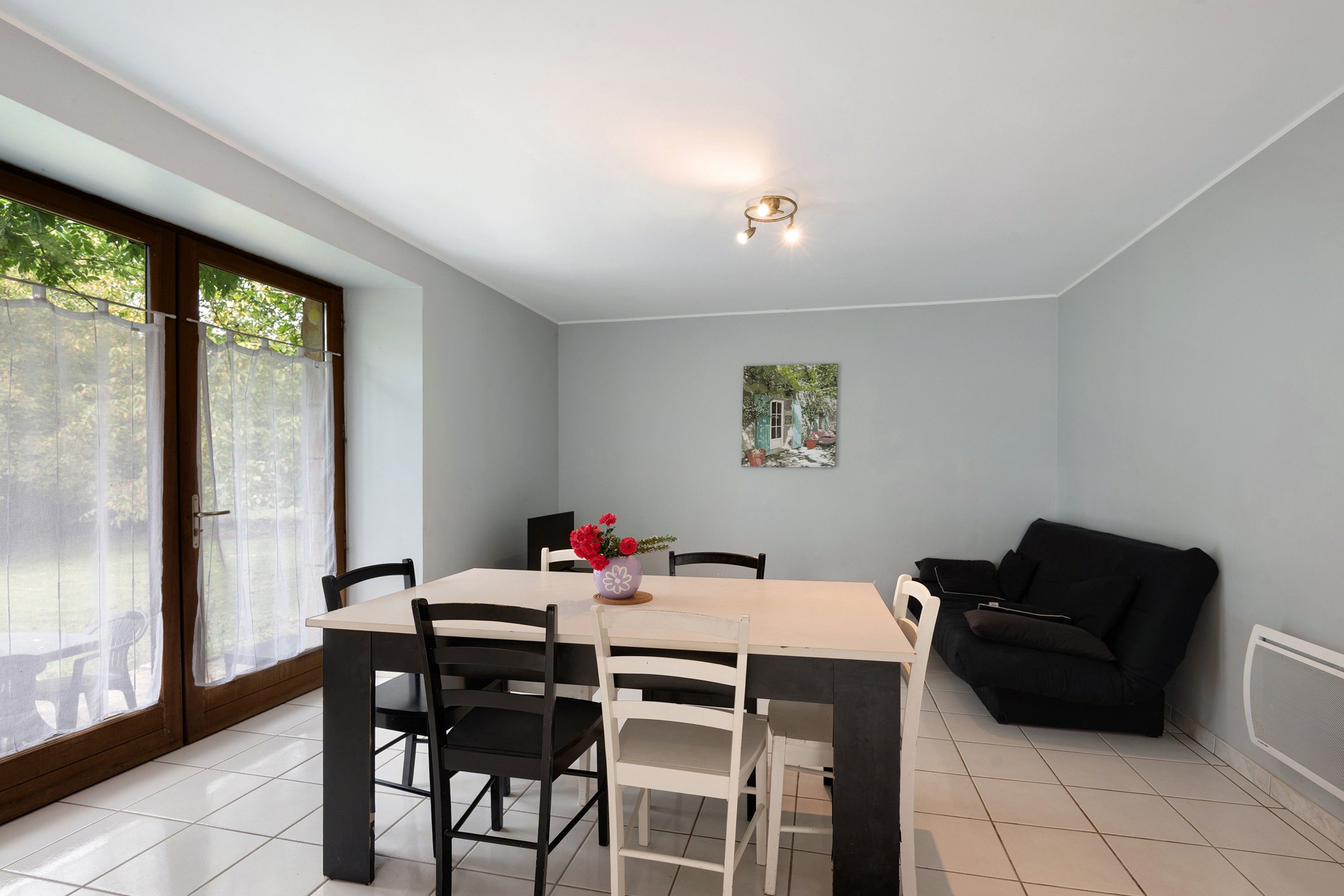 Un comedor con una mesa, sillas, un sofá negro y un cuadro en la pared.