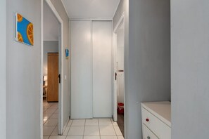 A narrow hallway with a white door at the end, a wooden door to the left, and a red bucket on the right.
