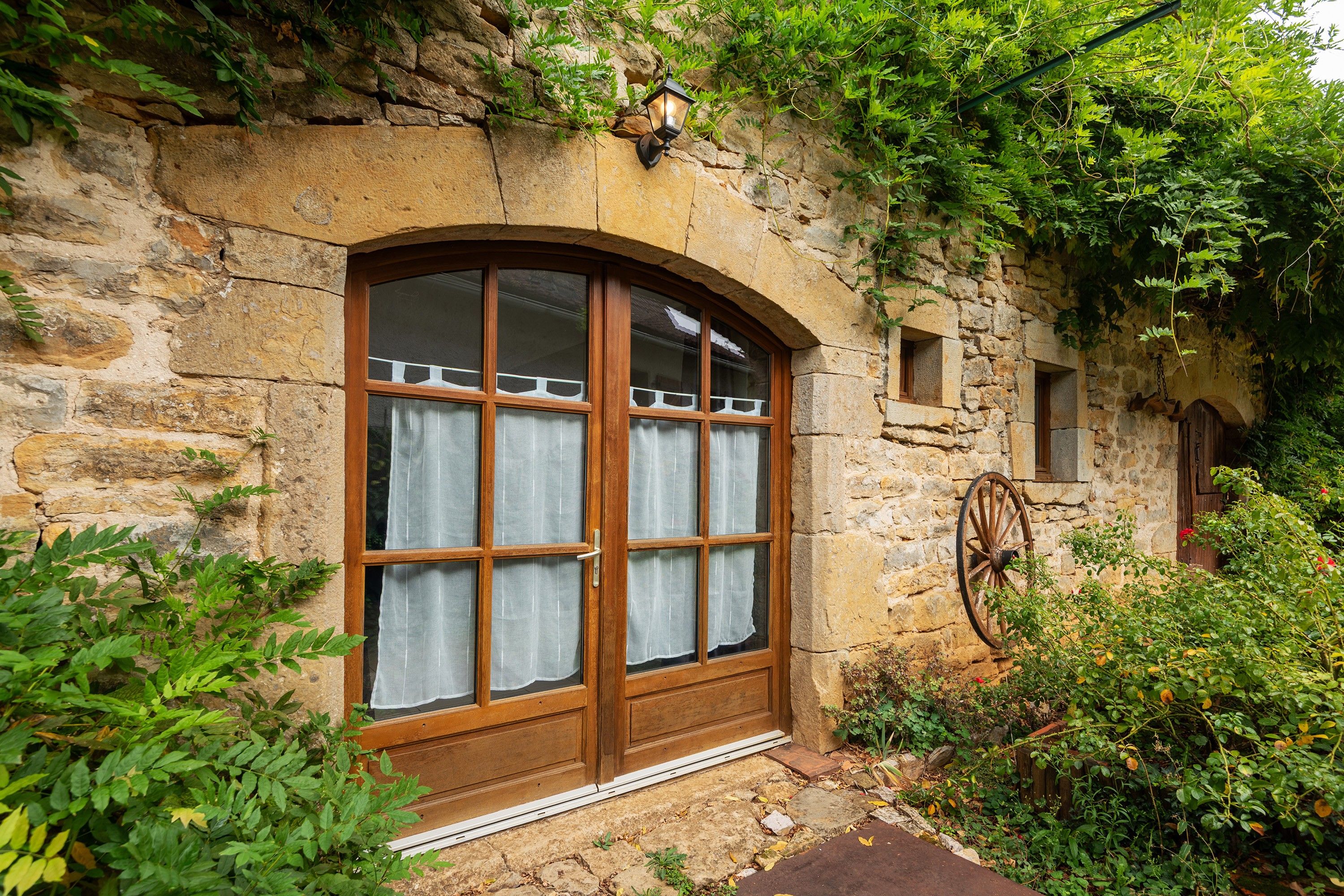 Un bâtiment en pierre doté d’une grande fenêtre en arc de cercle, d’une petite fenêtre et d’une roue en bois.