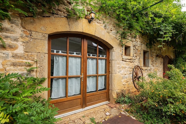 A stone building with a large arched window, a small window, and a wooden wheel.