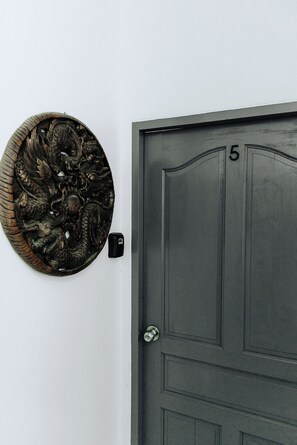 Una porta de fusta fosca amb el número 5, una placa decorativa penjada a la paret amb un disseny de drac i un timbre.