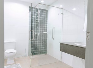 A modern bathroom with a glass-enclosed shower, a toilet, and a sink with a countertop. - The One Apartment (rawai)