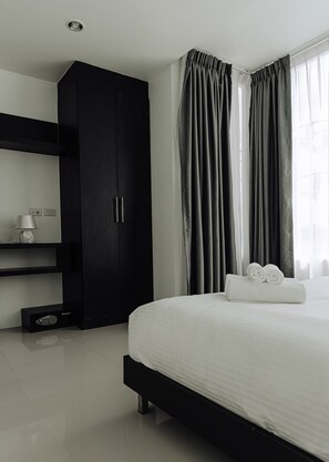 A modern hotel room with a large bed, a wardrobe, a bedside table with a lamp, and a window with curtains. - The One Apartment (rawai)