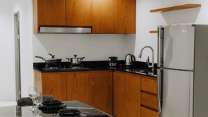 A compact kitchen with wooden cabinets, a stainless steel refrigerator, and a dining table set for two. - The One Apartment (rawai)