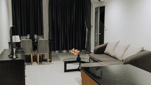 A modern living room with a sofa, a coffee table, a dining table with chairs, and a black curtain backdrop. - The One Apartment (rawai)