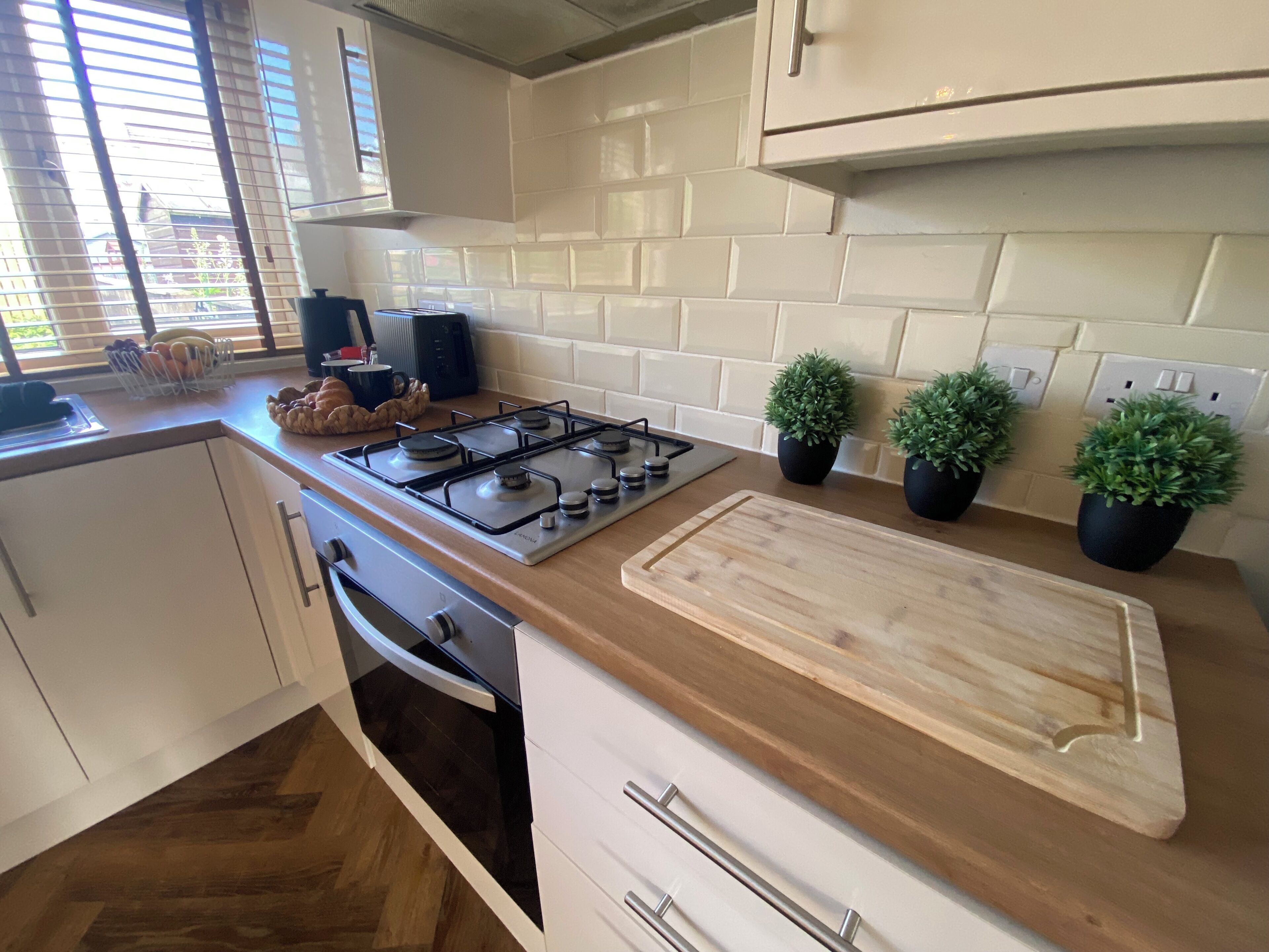 Une cuisine équipée d’une cuisinière à gaz, d’un plan de travail en bois, de plantes en pot et de meubles de rangement blancs.