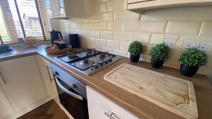 A kitchen with a gas stove, wooden countertop, potted plants, and white cabinetry.