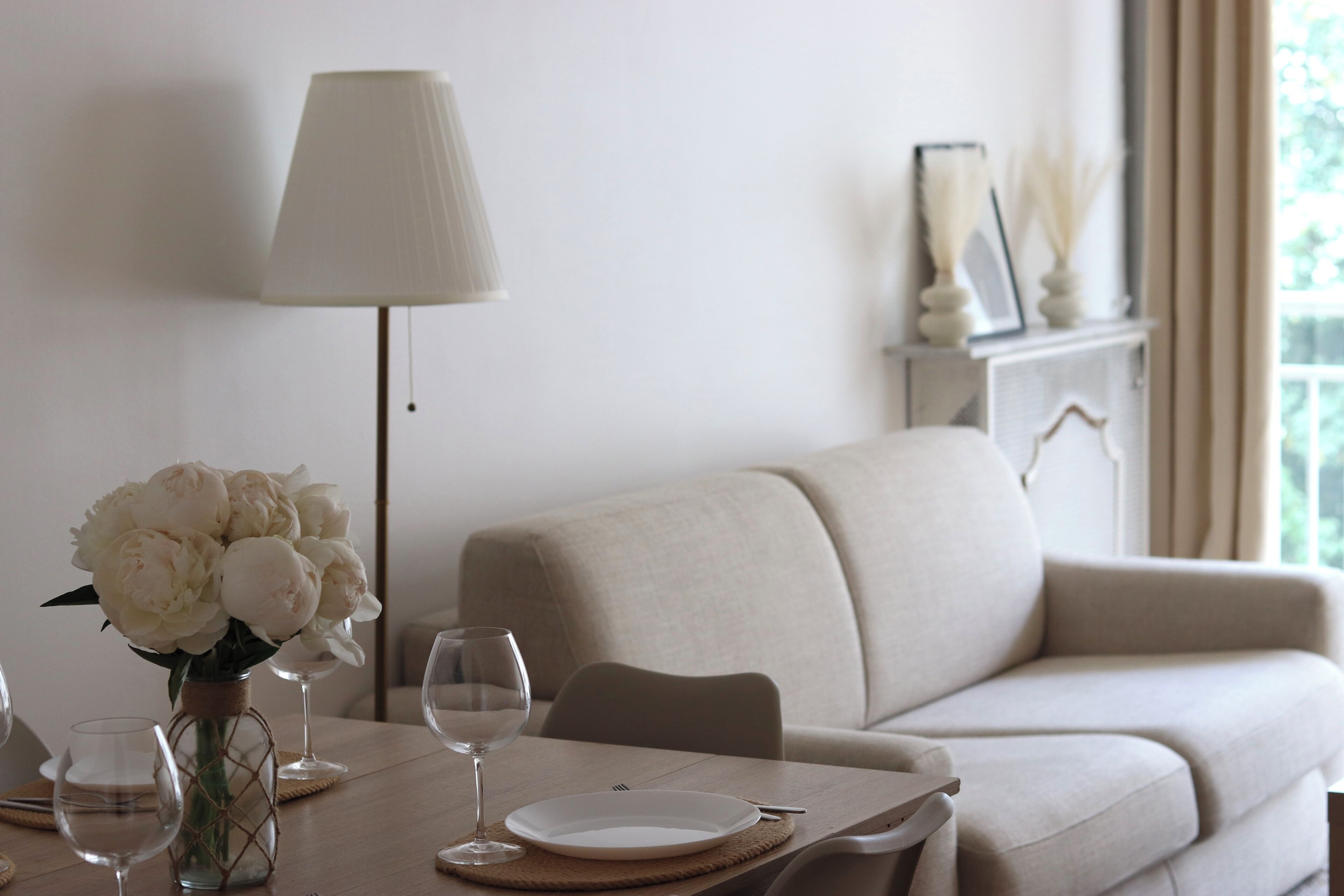 A dining area with a table set for two, a vase of flowers, and a lamp.