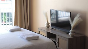 Hotellihuone, jossa on sänky, televisio puisen jalustan päällä ja ikkuna, jossa on verhot.