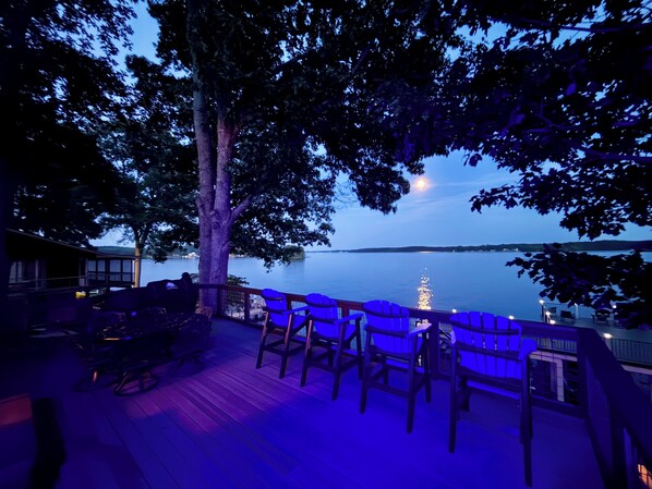 A deck with outdoor seating, a large tree, and a view of a calm lake at dusk. - 4 Bedroom, 2 Bath, Located on Main Lake, with Boathouse, Boat Slips, Sleeps 11 (Henrico)
