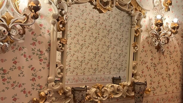 A mirror with ornate gold and white frame, floral wallpaper, and wall sconces. - Vacation Apartment in a Country House in a Quiet Setting in the Elm-Lappwald Recreation Area (Frellstedt)