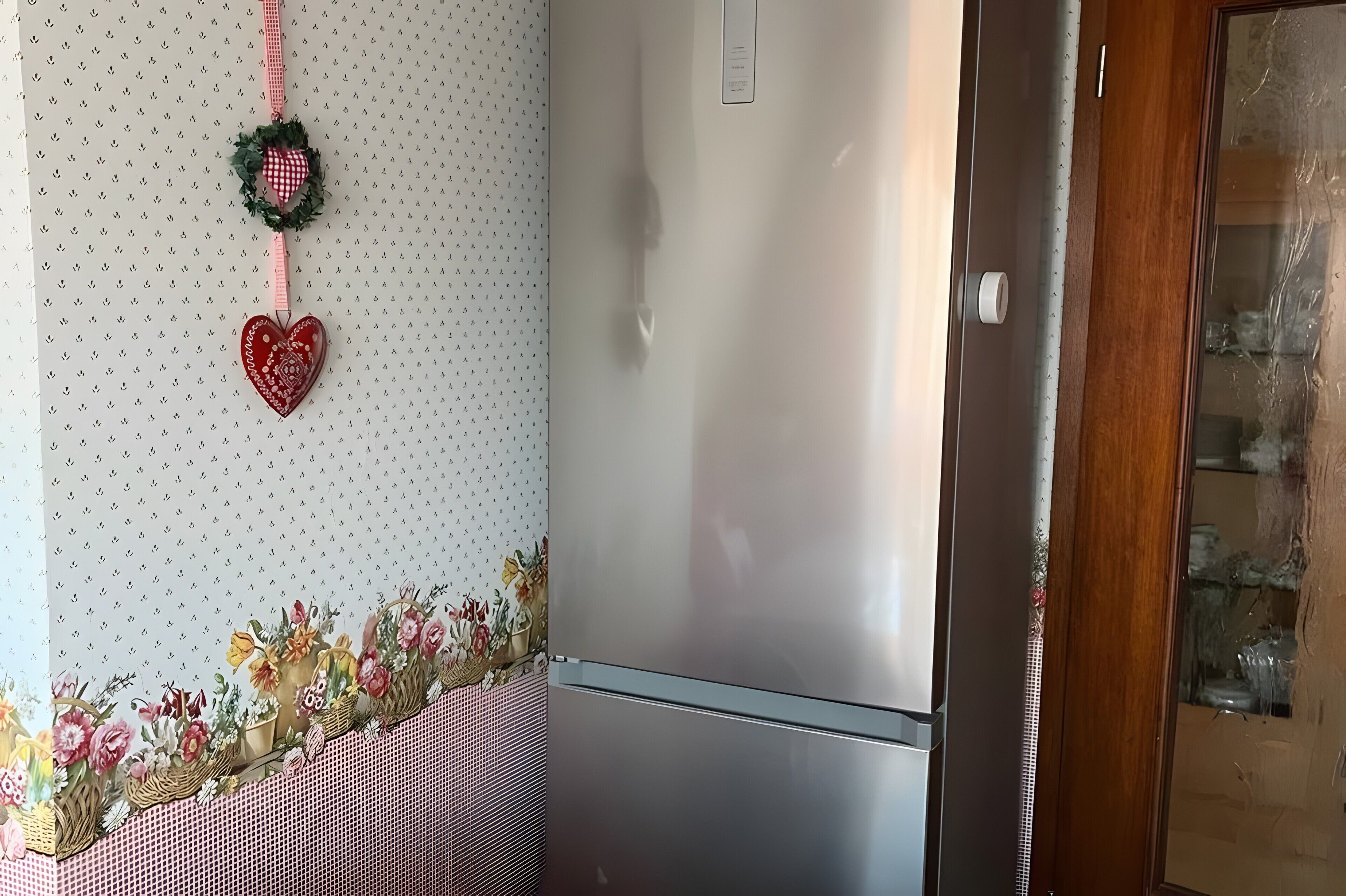 A kitchen with a refrigerator, a patterned wall, and a floral arrangement on the counter.