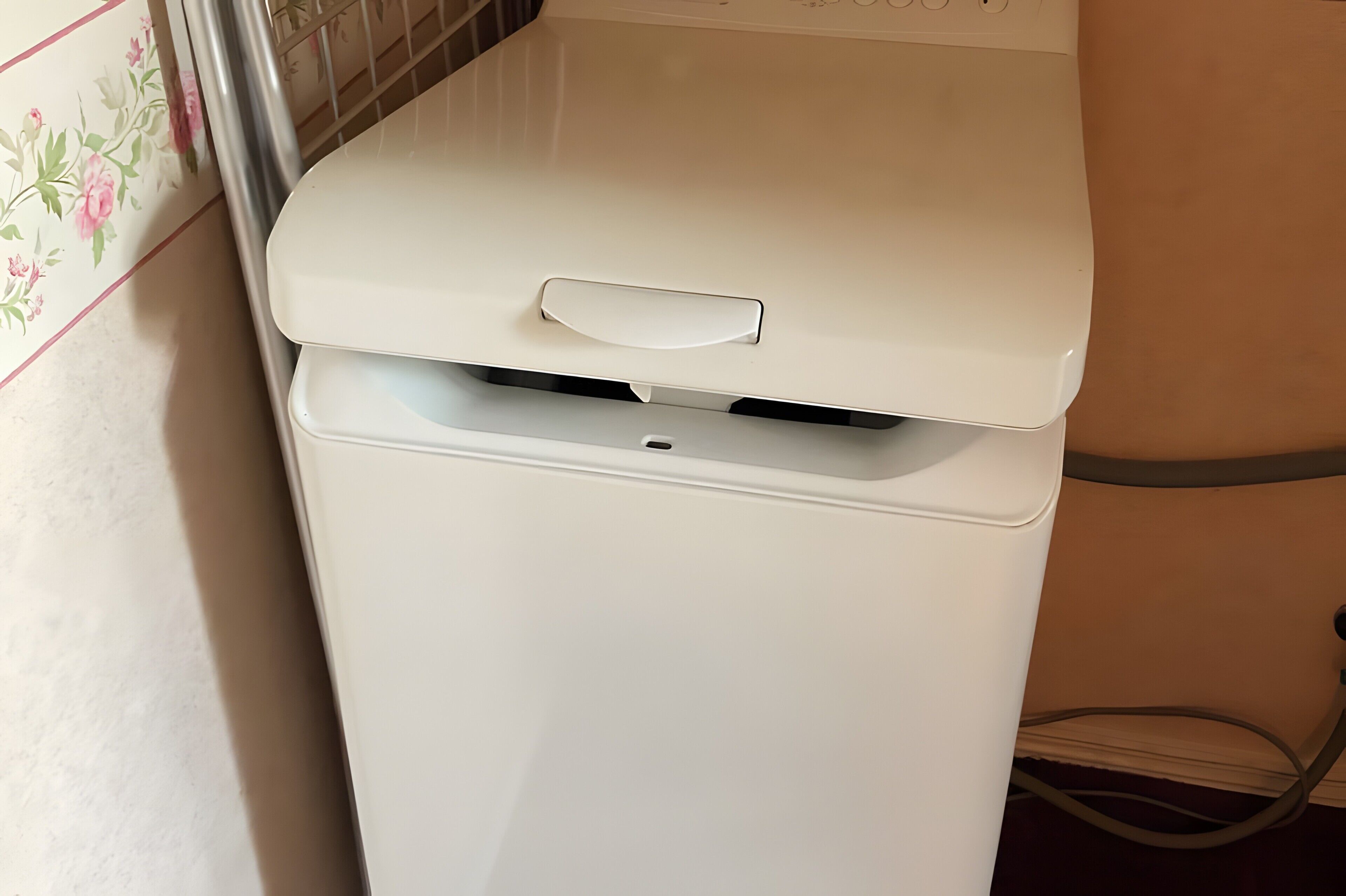 Een witte wasmachine met een handvat aan de bovenkant, in een ruimte met betegelde wanden.