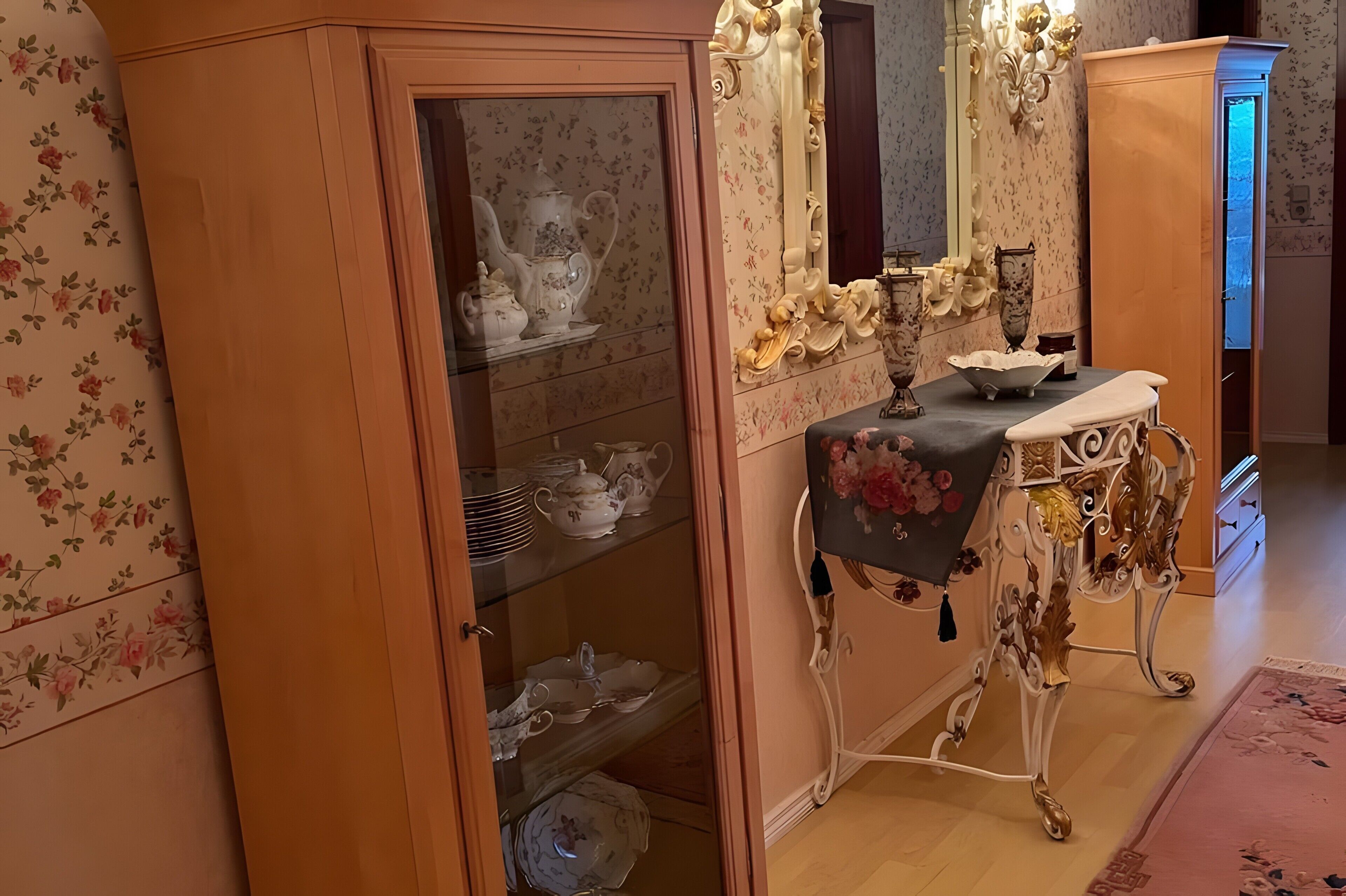 A room with a wooden cabinet, a mirror, and a table with floral decorations.