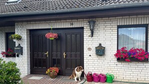 A house with a double door, a small porch, and a dog sitting by the door. - Vacation Apartment in a Country House in a Quiet Setting in the Elm-Lappwald Recreation Area (Frellstedt)