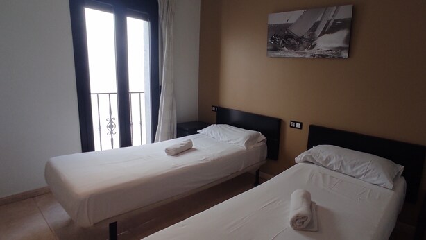 Una habitació d'hotel amb dos llits individuals, una finestra gran amb cortines i un quadre penjat a la paret.