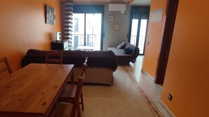 Una habitació amb taula de dinar de fusta, sofà, llit i finestra amb vista a l'exterior.