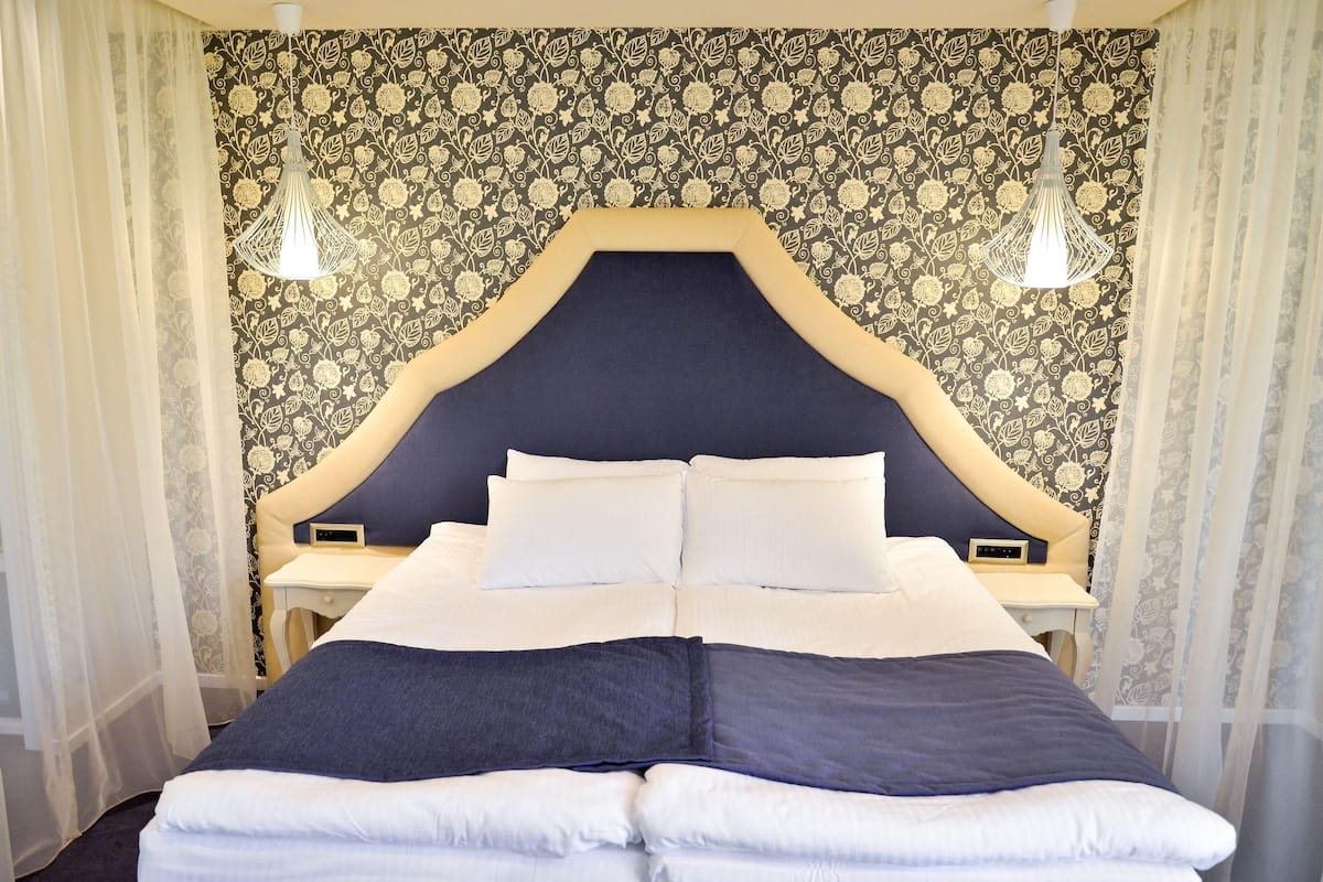 Una cama bien hecha con cabecera, dos mesitas de noche y una pared con estampado floral.
