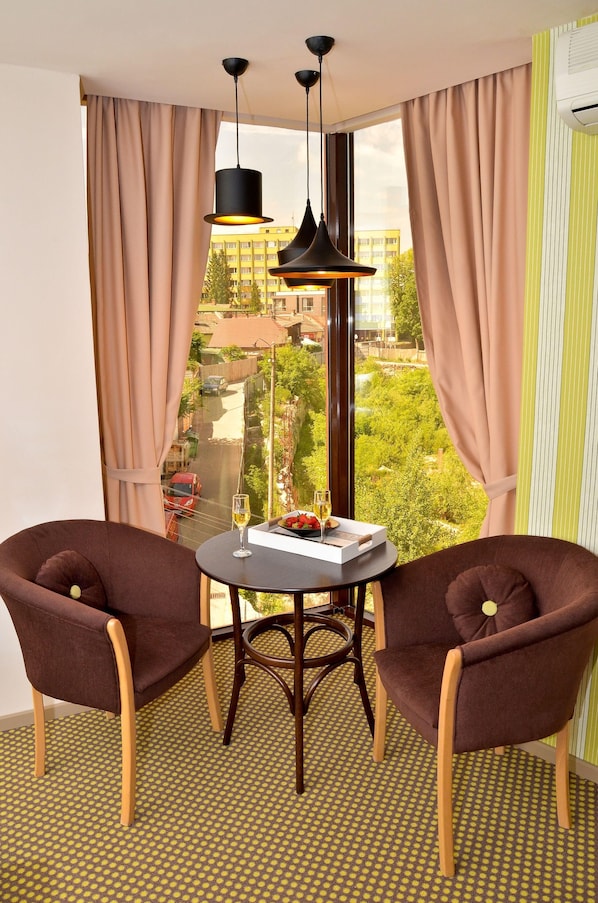 A room with two brown armchairs, a small round table with a glass of wine, and a view of a cityscape through large windows.
