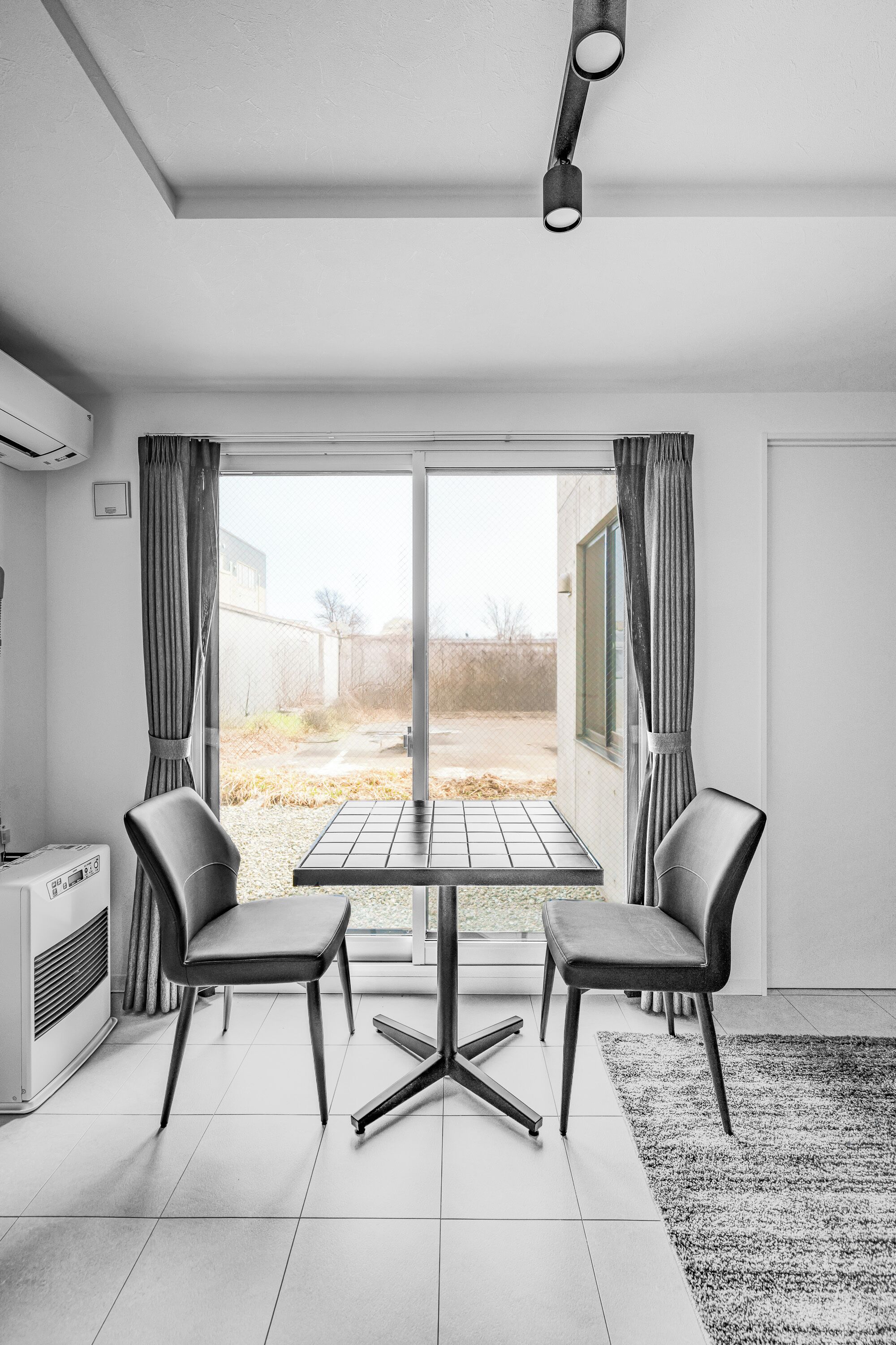 A modern room with a dining table and chairs, a large window with curtains, a radiator, and a ceiling light fixture.