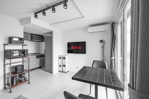 Una cuina moderna amb microones, torradora i cafetera sobre un carretó, taula de menjador amb un panell solar, televisió penjada a la paret i finestra amb cortines.