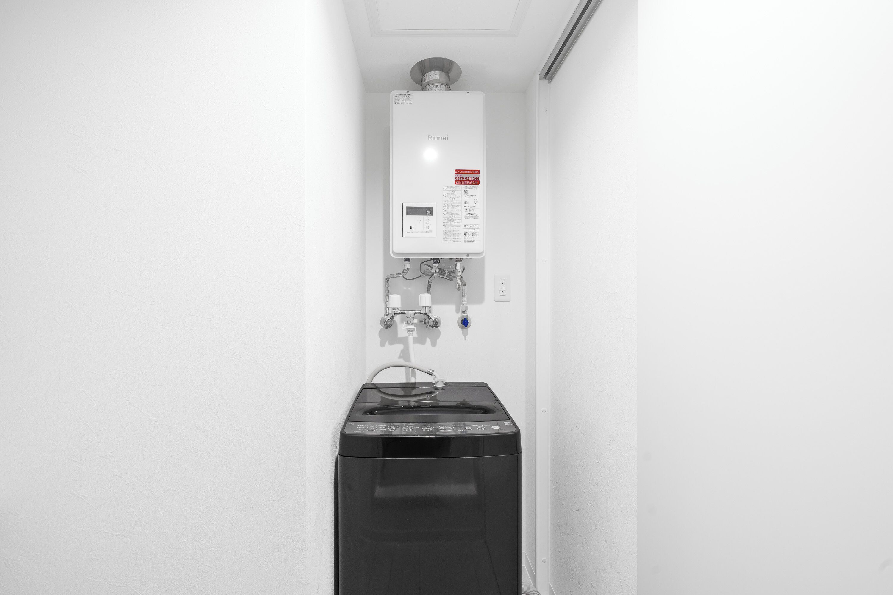 A white wall with a water heater and a black appliance, possibly a washer or dryer, in a corner.