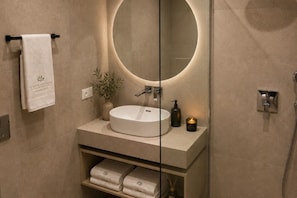 A modern bathroom with a round mirror, a white sink, a shelf with folded towels, and a small plant. - Mayiva Royal House Center Hvar (Hvar)