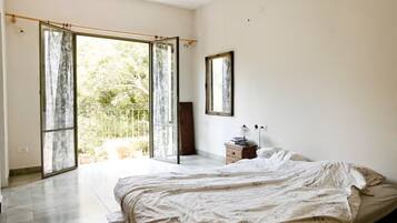 Une chambre à coucher comprenant un lit, une table de chevet, un miroir et une porte-fenêtre coulissante donnant sur un balcon.
